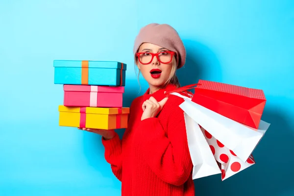 一个年轻女孩的肖像在红色毛衣与礼品盒和购物袋的蓝色背景 — 图库照片