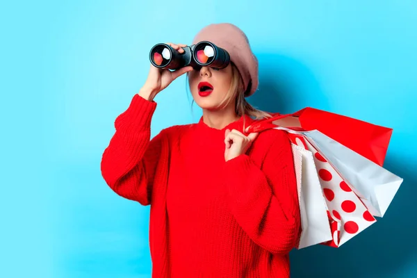 Bonocular 상자와 쇼핑백 파란색 배경에 빨간색 스웨터에 여자의 초상화 — 스톡 사진