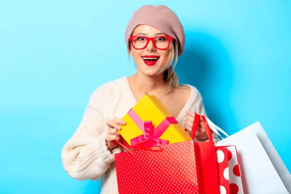 一个年轻女孩的肖像在白色毛衣与礼品盒和购物袋的蓝色背景 — 图库照片