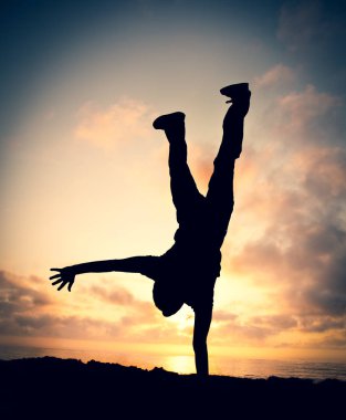 Genç adam akrobasi sahilde günbatımı sırasında gerçekleştirir