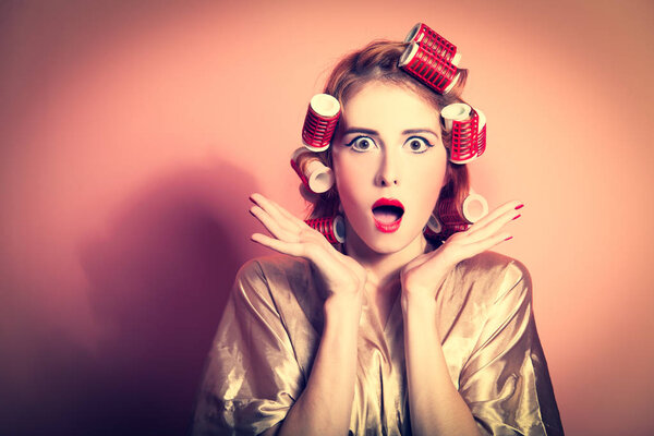 Удивлённая домохозяйка с бигудями на розовом фоне
