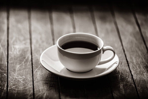 White cup of tea with saucer on wooden table. Image in black and white color style
