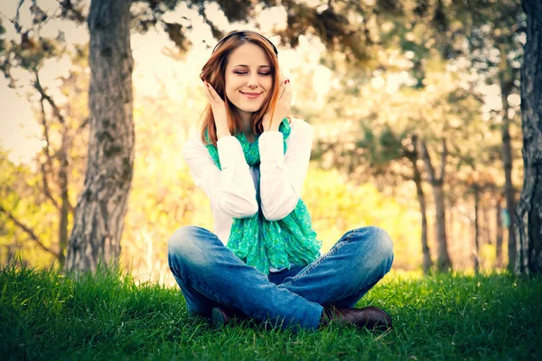 公園の芝の上に座ってヘッドホンで赤毛の女の子 — ストック写真