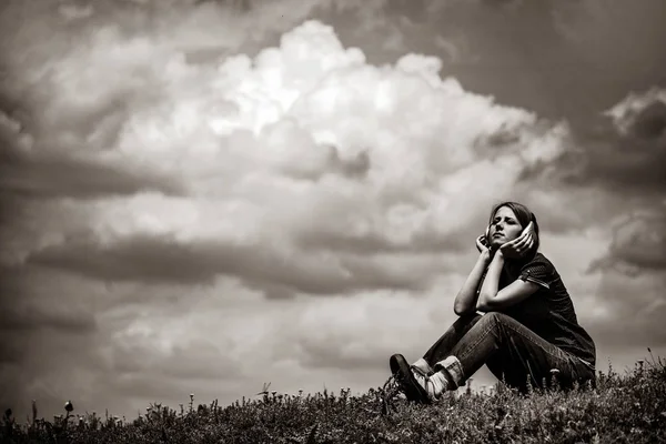 草原に座ってヘッドフォンを持つ少女 黒と白の色のイメージ — ストック写真