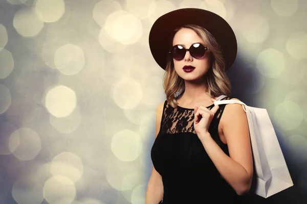 灰色の背景にボケ味のショッピング バッグと黒のドレスと帽子で若いスタイルの女の子の肖像画 — ストック写真