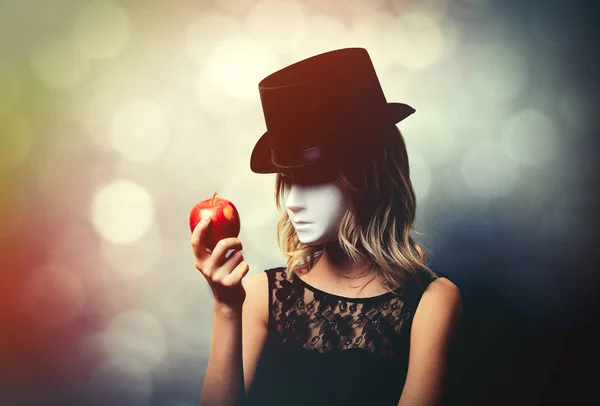一个年轻的女孩在顶帽子和白色面具与苹果在灰色背景的肖像 — 图库照片