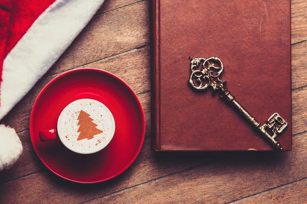 红杯卡布奇诺与钥匙和书附近的圣诞节帽子在木桌上 — 图库照片