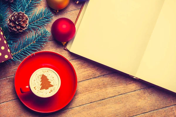 红杯卡布奇诺与奶油圣诞树和打开书在木桌附近的玩具 — 图库照片