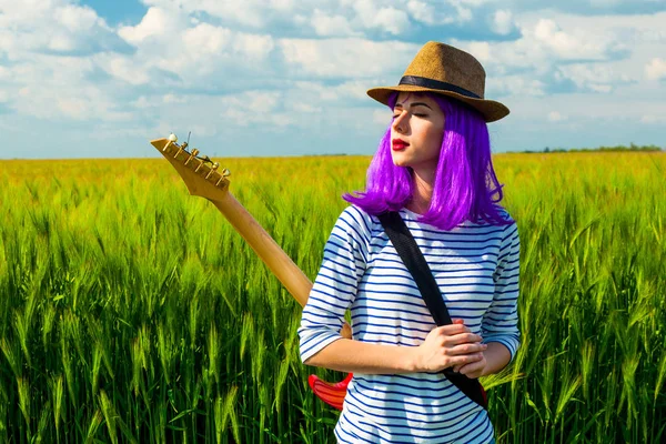 Молодая женщина с гитарой возле поля — стоковое фото