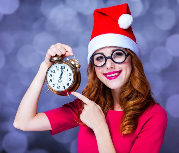 Girl in christmas hat and glasses with alarm clock — Stock Photo, Image