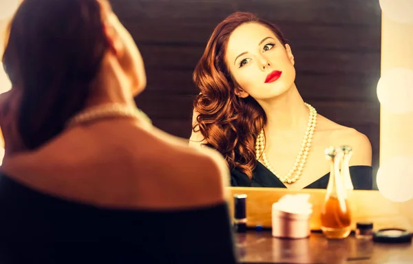 Retrato de una mujer hermosa como la aplicación de maquillaje cerca de un espejo — Foto de Stock