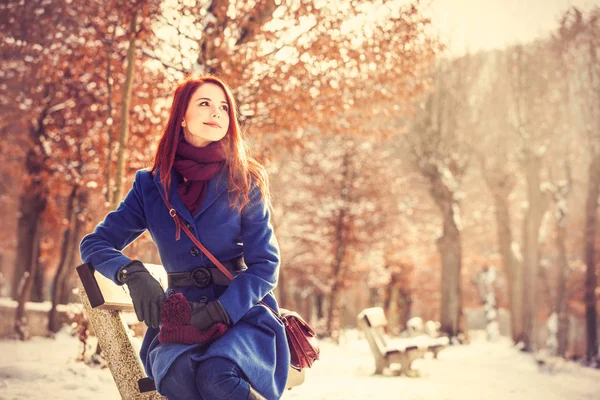 Meisje zittend op een bankje in het park van de winter. — Stockfoto