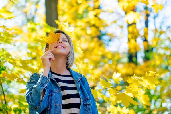 ブルー ジーンズ服の美しい金髪少女秋シーズンの時間に公園の残りがあります — ストック写真