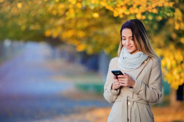 Sonbahar sezonu sokak üstünde hareket eden telefon ile genç kız 