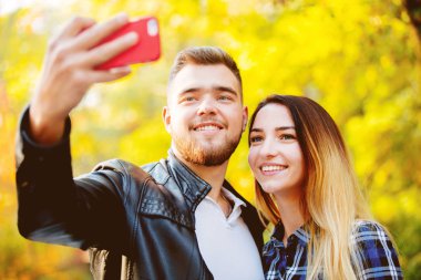 Genç beyaz bir selfie üstünde hareket eden telefon ile sarı arka plan ağaçta bir parkta çiftsiniz. Sonbahar sezonu zaman 