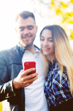 Cep telefonunuzun ve arka planda sarı ağaçları ile bir parkta Genç beyaz çift. Sonbahar sezonu zaman