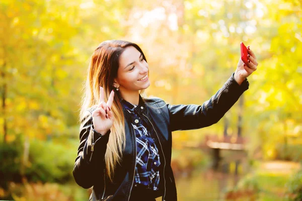 小さなホワイト女の子の背景に黄色の木がある公園で Selfie の携帯電話のカメラを使用しています 秋シーズンの時間 — ストック写真