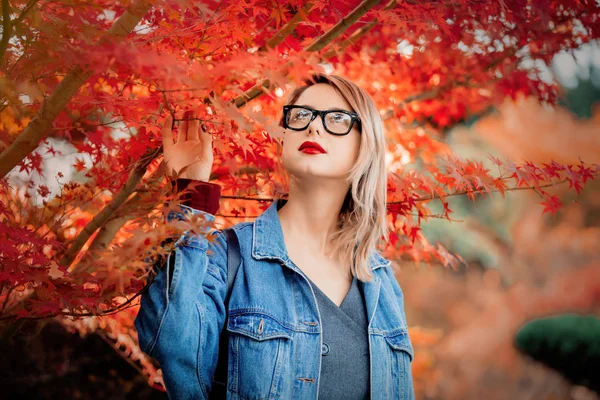 公園で眼鏡と青のデニム ジャケットでスタイリッシュな女性 秋シーズンの時間 — ストック写真
