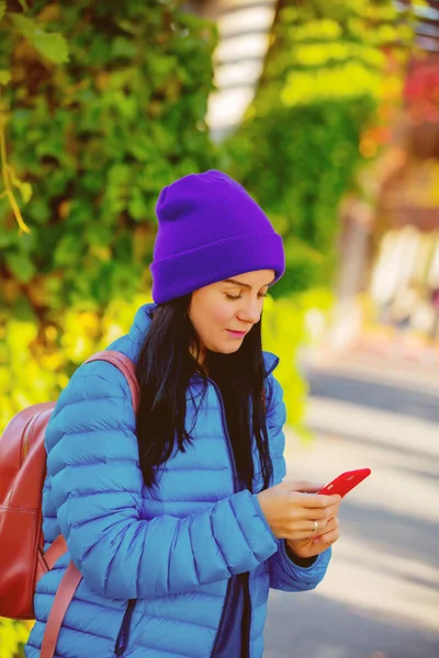 蓝色夹克的年轻女孩纵向在秋季的小巷使用手机的背包 — 图库照片