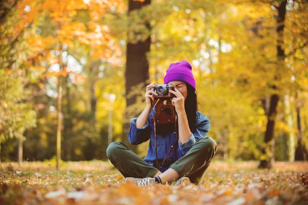 秋の公園でプロのカメラで写真を作る紫の帽子の若い女性 — ストック写真