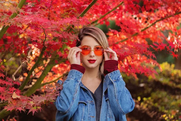 公園で眼鏡と青のデニム ジャケットでスタイリッシュな女性 秋シーズンの時間 — ストック写真