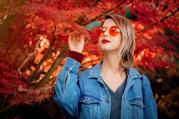 公園で眼鏡と青のデニム ジャケットでスタイリッシュな女性 秋シーズンの時間 — ストック写真