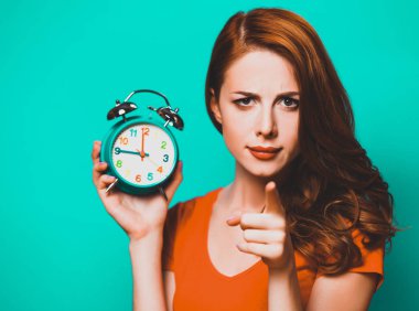 Kızıl saçlı kız mavi zemin üzerine çalar saat ile.