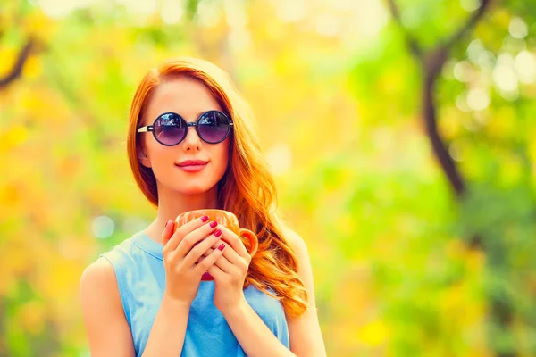微笑的红头发的女孩与杯子在秋天公园 — 图库照片