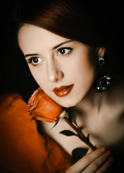 Portrait of a beautiful girl in a red dress holding a red rose near the face.