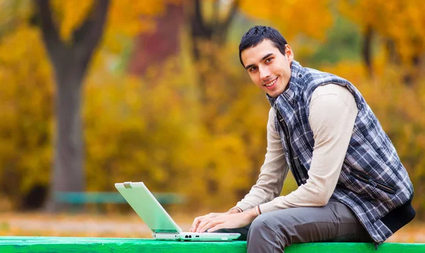 Programista z notebooka siedzi w parku jesień — Zdjęcie stockowe