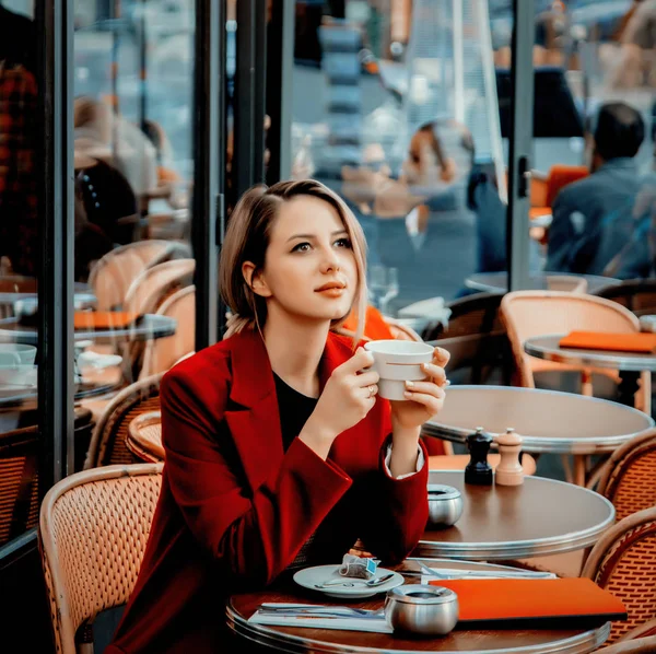 Girl in red coat with cup of coffee in parisian cafe — Stock Photo, Image