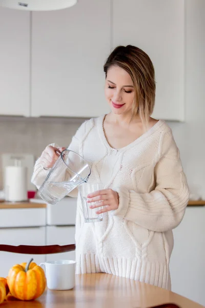 Chica joven en suéter con vaso de agua en la cocina —  Fotos de Stock