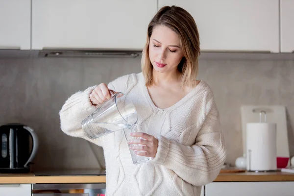 Młoda dziewczyna w sweter z szklanką wody w kuchni — Zdjęcie stockowe