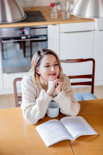 Girl in white sweater sitting at table with cup of coffee — Stock Photo, Image