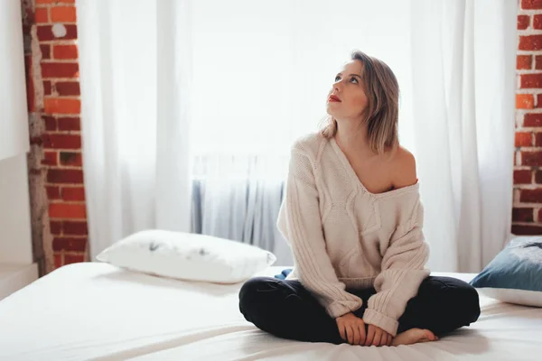 Jovem mulher de camisola branca sentada na cama — Fotografia de Stock