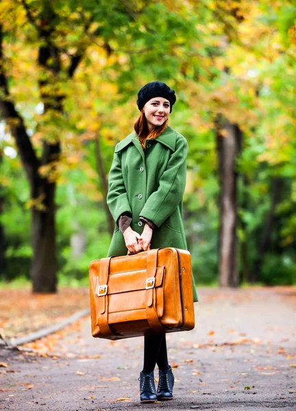 Стильная рыжая девушка в берете и пальто с чемоданом — стоковое фото