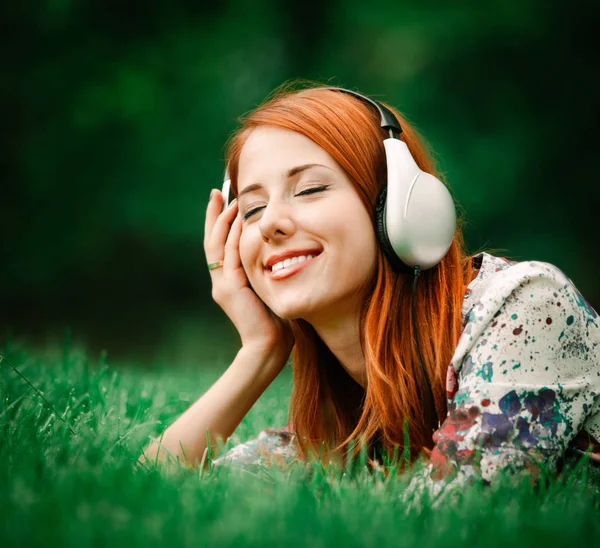 Pelirroja en los auriculares en el césped —  Fotos de Stock