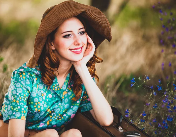 Chica pelirroja joven en sombrero y vestido con maleta — Foto de Stock