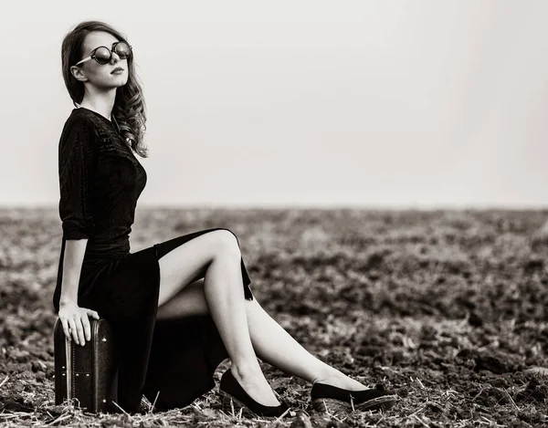 Woman sitting on suitcase at countryside — Stock Photo, Image