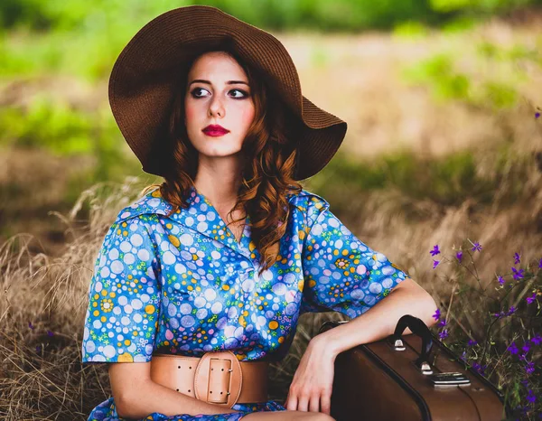 Chica pelirroja joven en sombrero y vestido con maleta — Foto de Stock