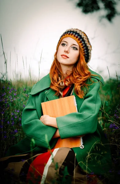 女孩拿着笔记本, 坐在绿草如茵 — 图库照片