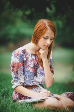 Kızıl saçlı kız yeşil çim üstünde defter ile