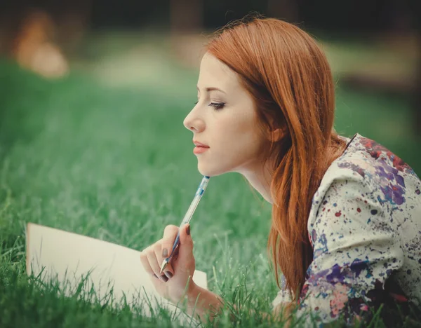 红头发的女孩与笔记本在绿色的草坪上 — 图库照片