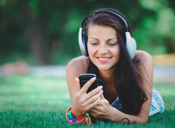 Woman with headphones lying down on green lawn — Stock Photo, Image