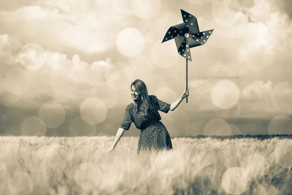 Девушка стоит на пшеничном поле с вертушкой — стоковое фото