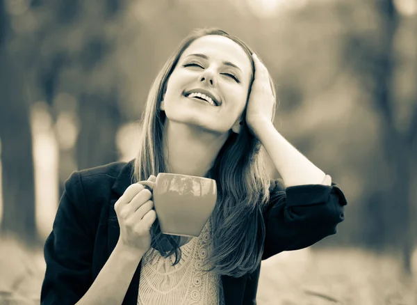 Flicka med kopp kaffe sitter på gräset i en park — Stockfoto