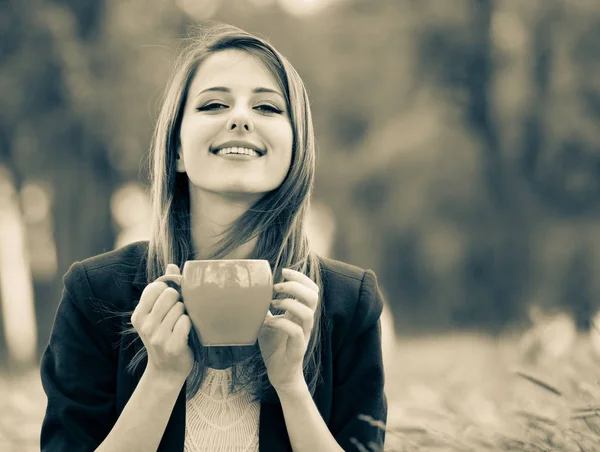 Flicka med kopp kaffe sitter på gräset i en park — Stockfoto