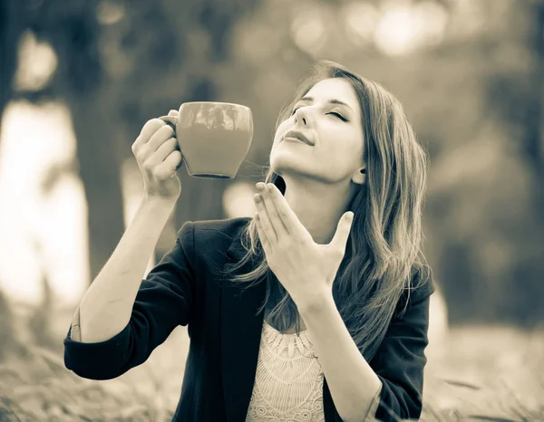 Девушка с чашкой кофе сидит на траве в парке — стоковое фото