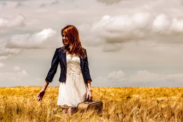 Rödhårig tjej med resväska på vetefält — Stockfoto