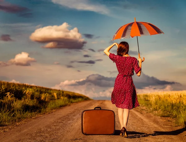 Девушка с чемоданом и зонтиком просыпается на дороге — стоковое фото